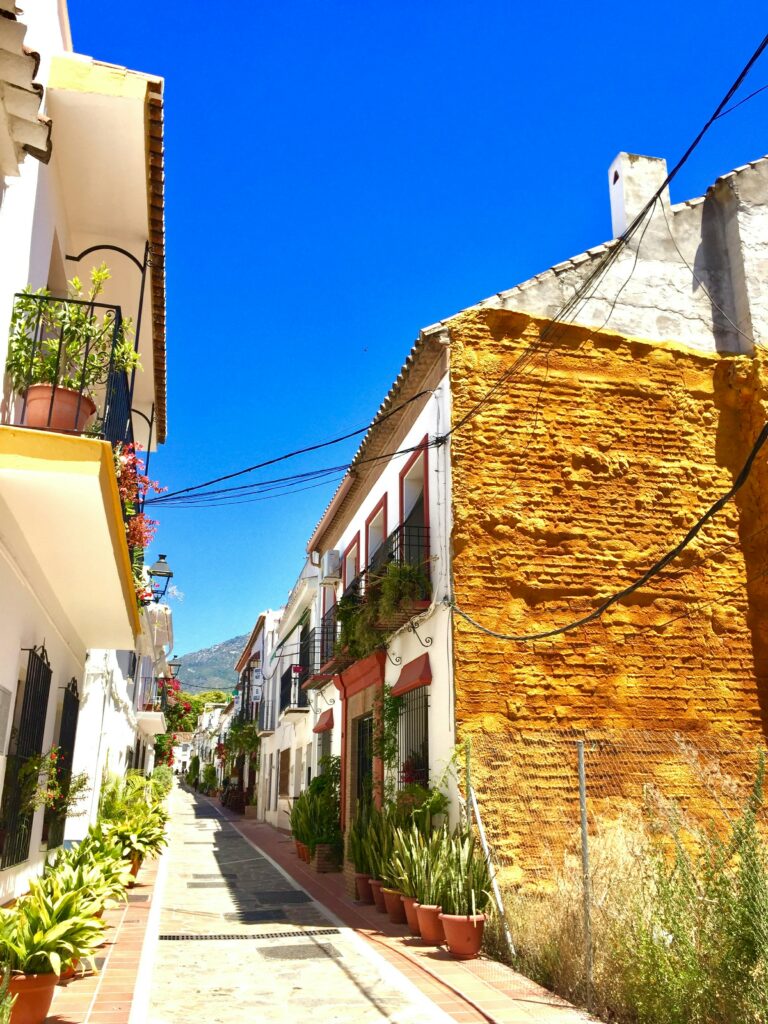 A picturesque narrow street in Marbella's Old Town, lined with traditional white houses, vibrant plants, and a cobblestone path leading towards the mountain